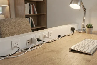 Prise intégrée dans une goulotte électrique blanche fixée sur un bureau de télétravail moderne avec câbles bien organisés
